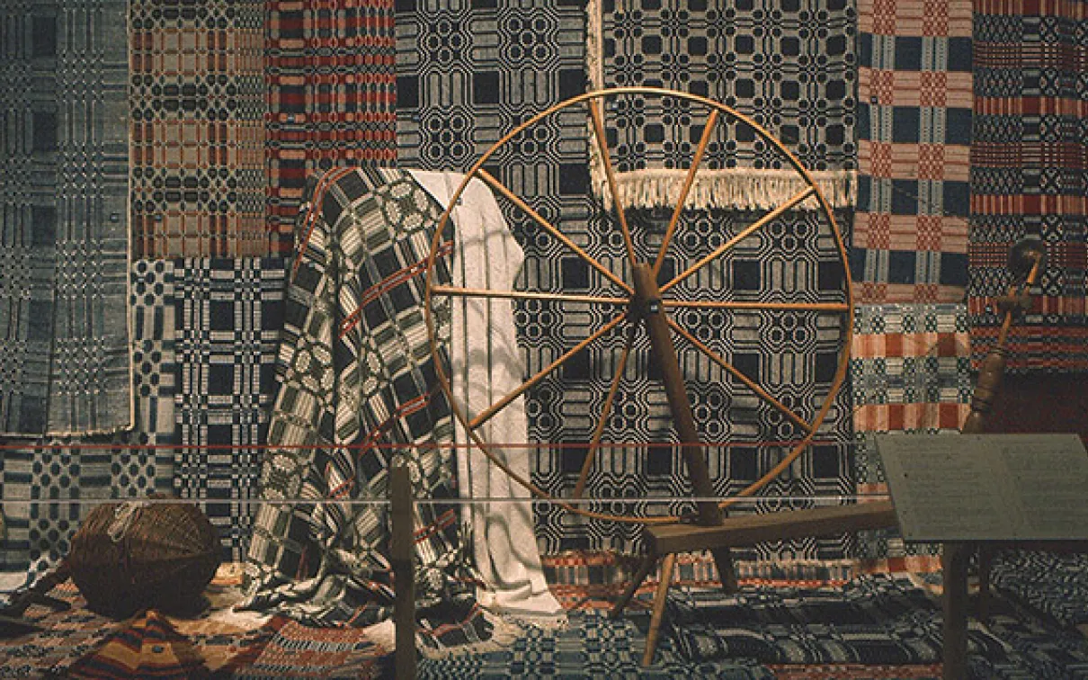 Photograph of <em>Keep Me Warm One Night</em>, the exhibition.
 Photograph of textiles behind a spinning wheel