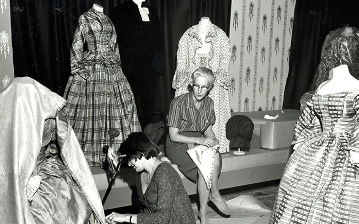 Black and white photo of Dorothy Burnham mounting a costume in the museum.
