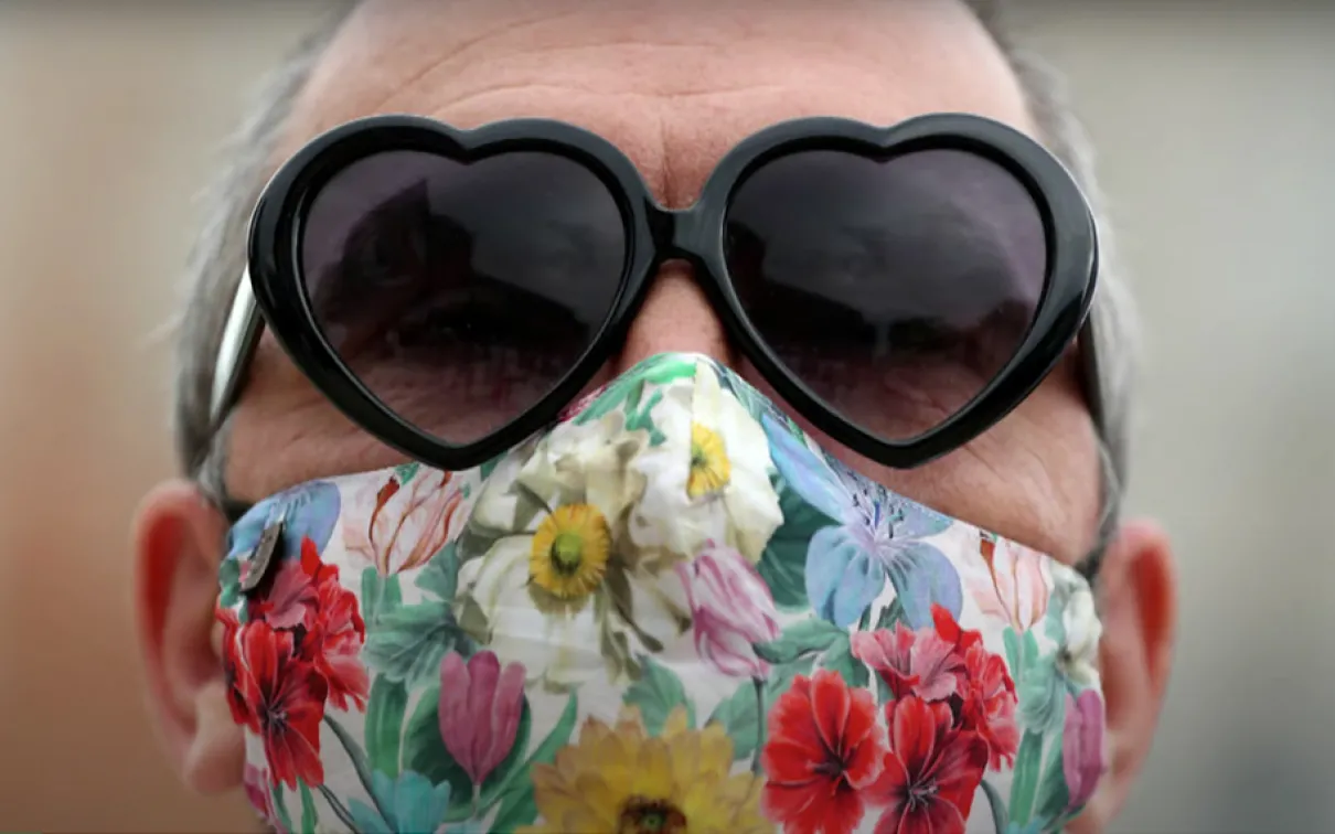 Woman wearing heart-shaped sunglasses and floral face mask.
