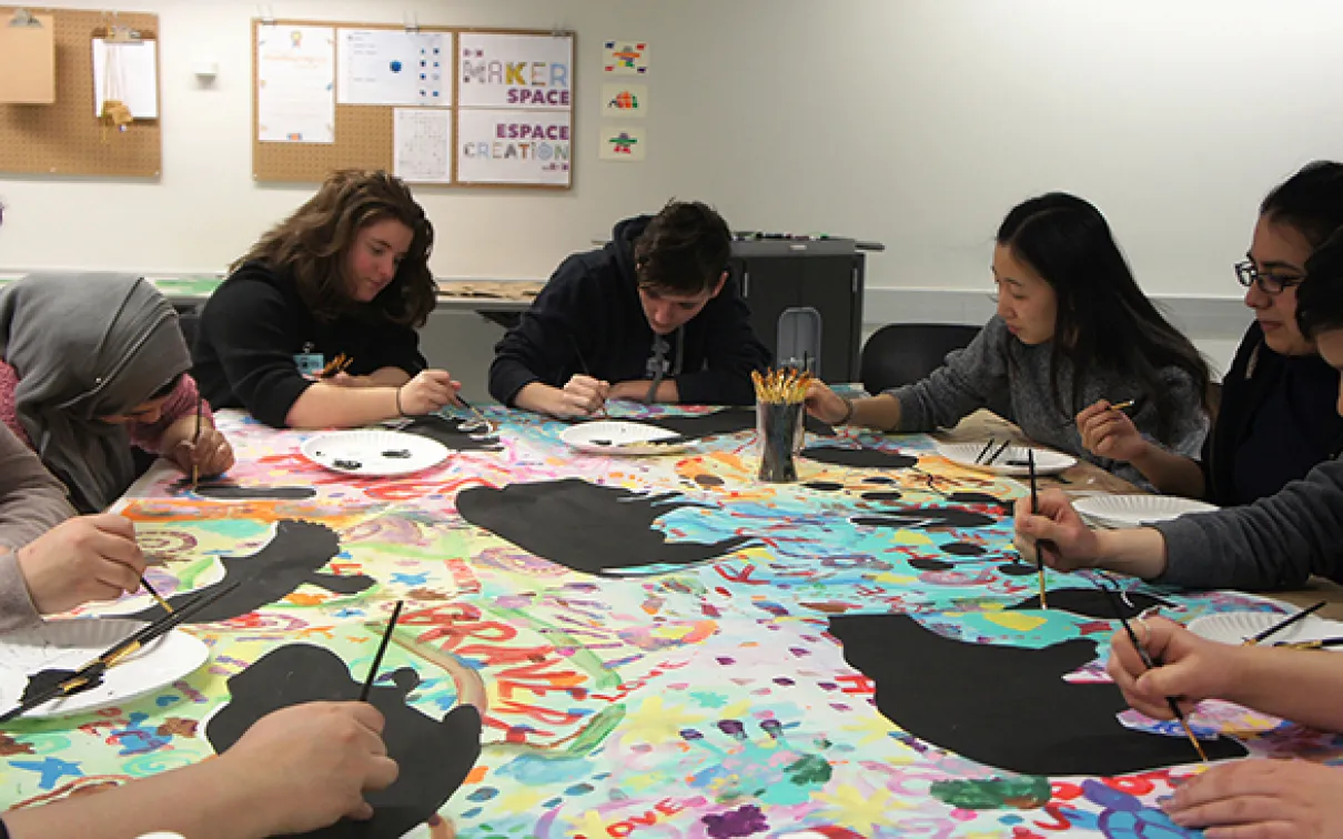 Un groupe de membres du Cabinet des jeunes peint sur une toile à une table.
