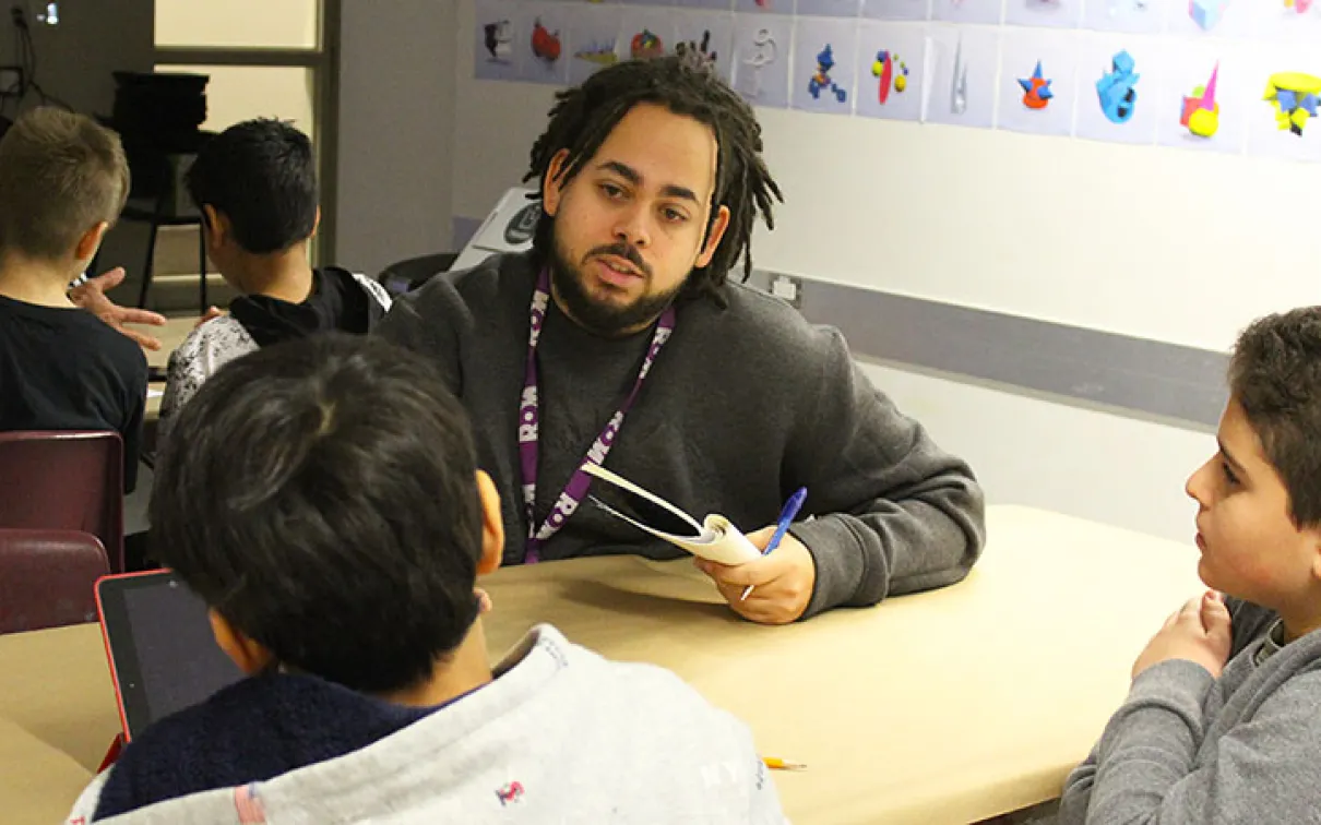 ROM intern talking with two elementary school students at a table
