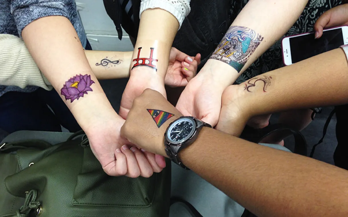 Six students show off their tattoo designs on their arms
