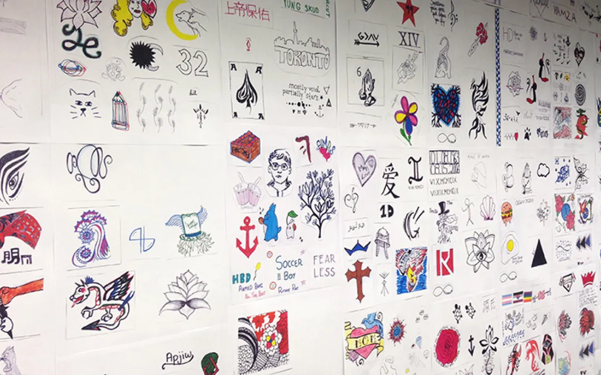 Des centaines de dessins de tatouage sur papier blanc sont affichés sur un mur.
