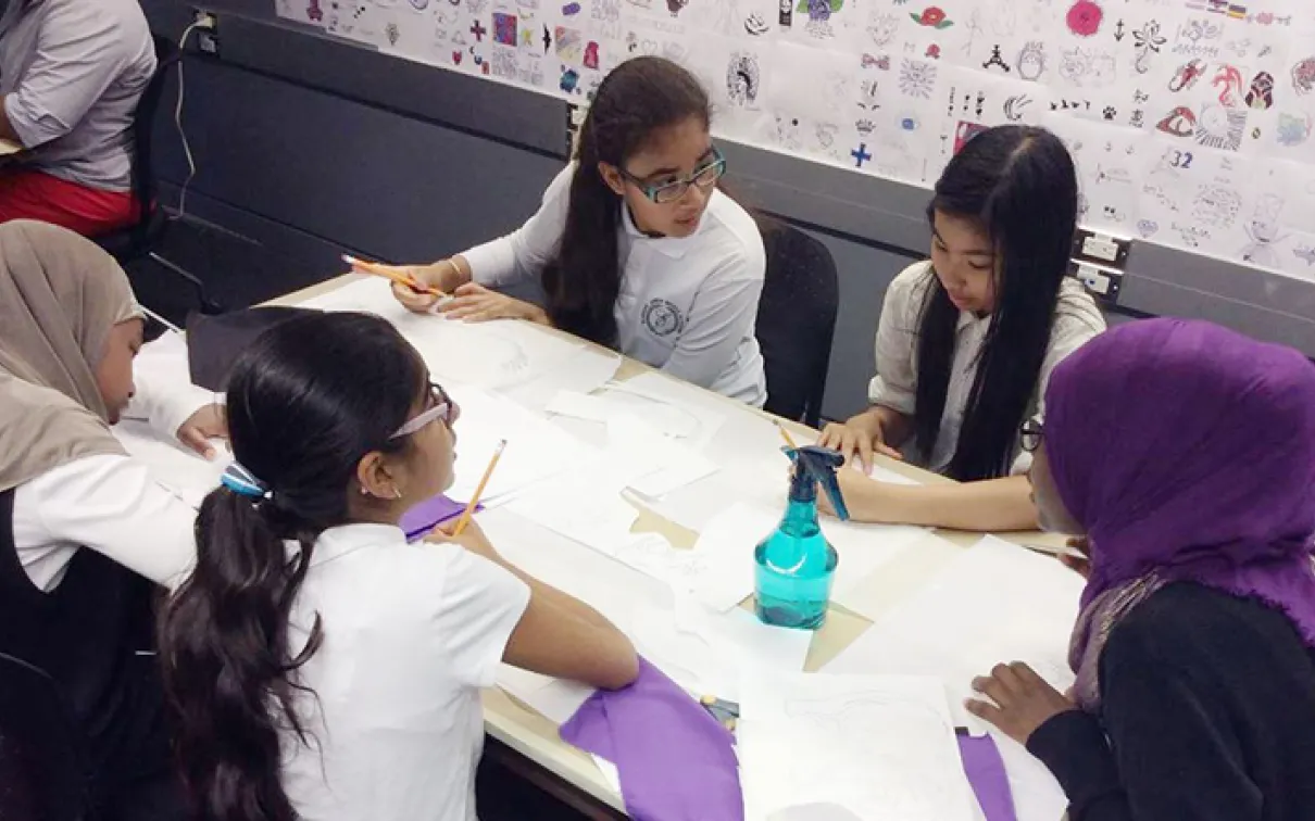 Five students around a table trace flag applique designs onto fusible interfacing fabric
