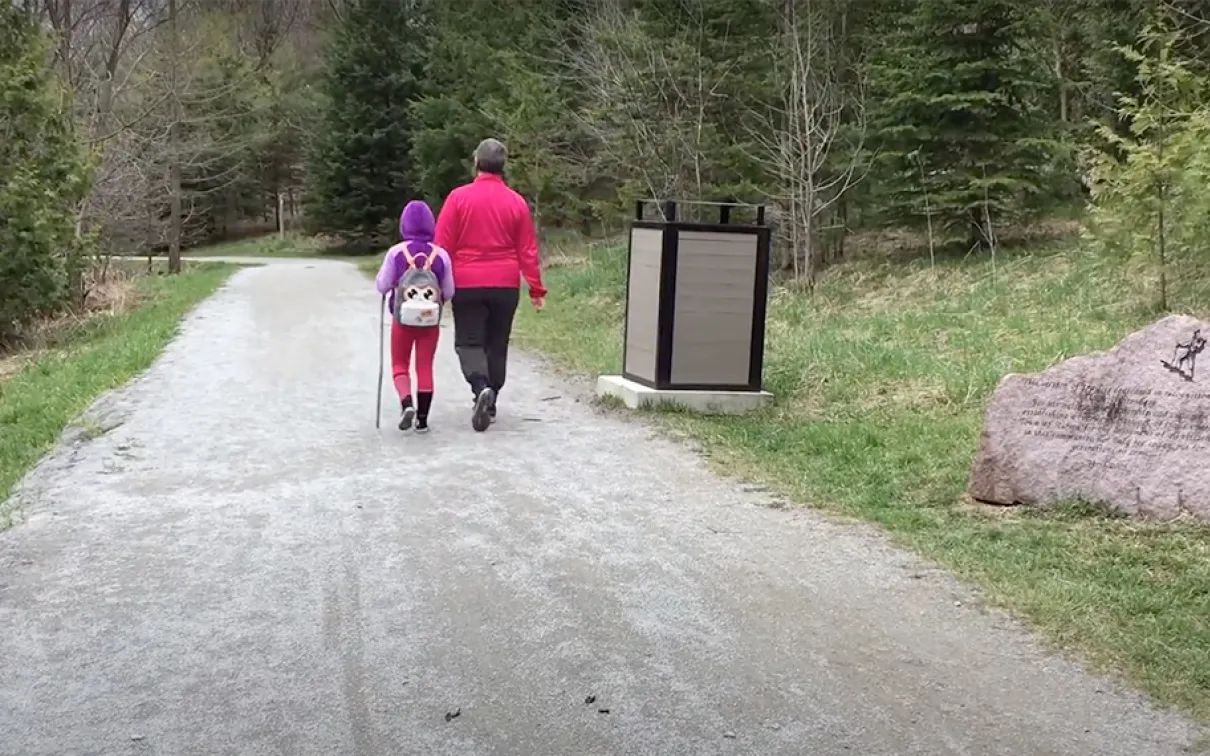 Woman and child walking along a trail path into a forest.
