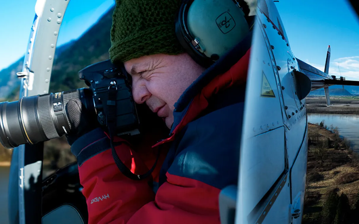 Andrew Wright taking a photograph in a helicopter.
