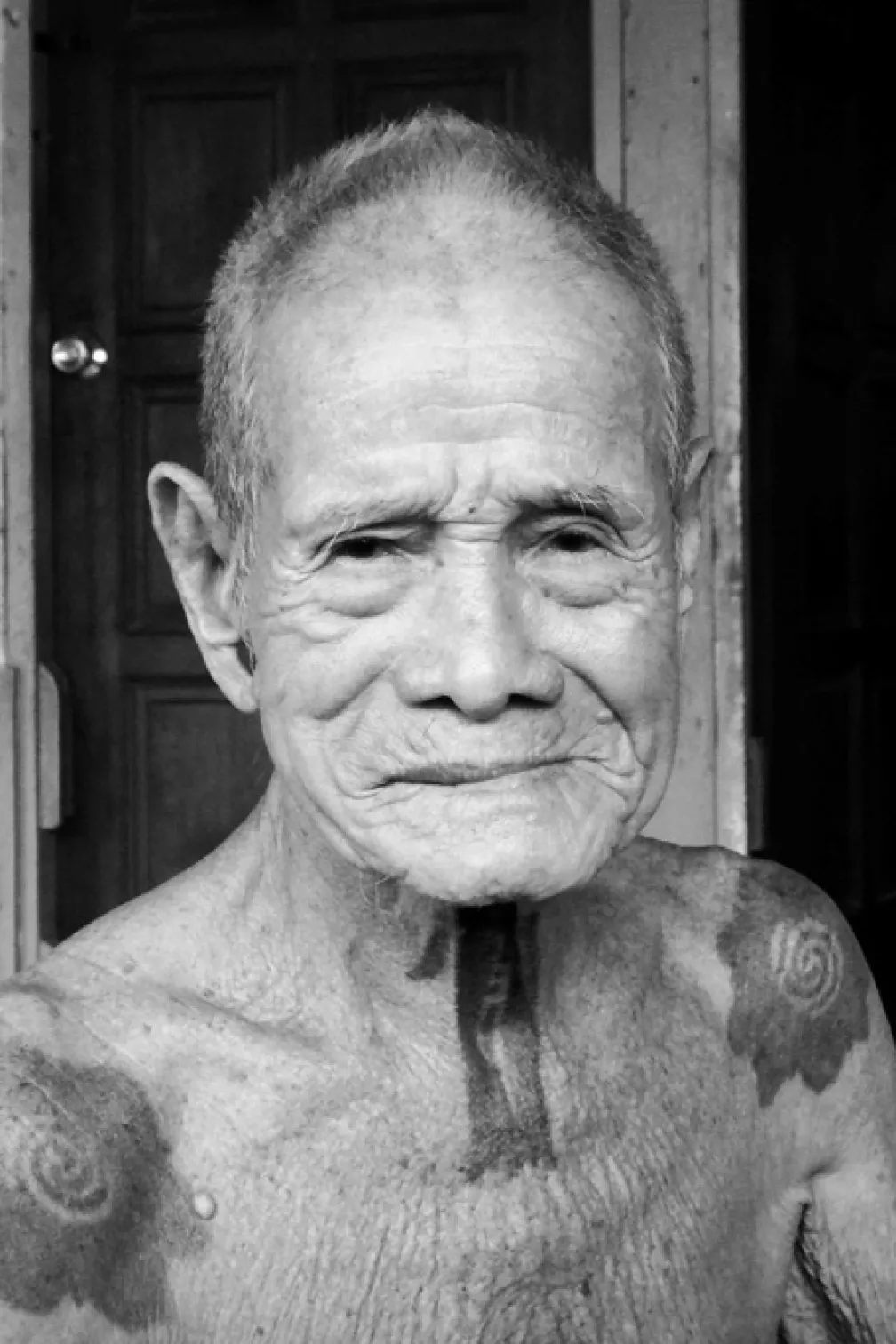 An Iban elder at Nanga Beretik longhouse.
 Black and white photograph of an older man with tattoos on his neck and shoulders