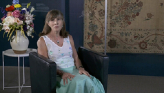 Deborah Metsger sitting in front of floral tapestry.