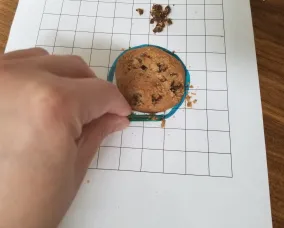 Chocolate chip cookie on grid paper, pile of chocolate chips beside it. Paperclip moving cookie fragments back into the original cookie outline.