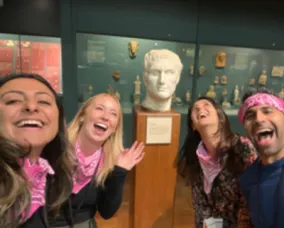 Four visitors laughing and smiling while standing in front of a Greek marble bust.