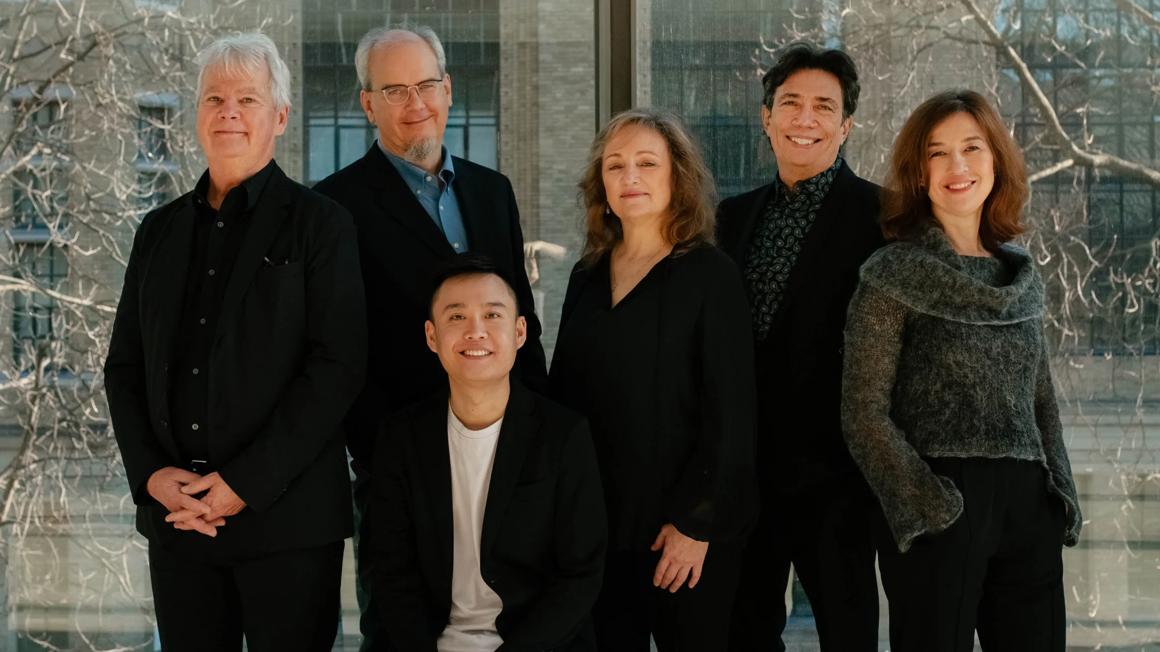 Six musicians in dark clothing, gathered in a group photograph.