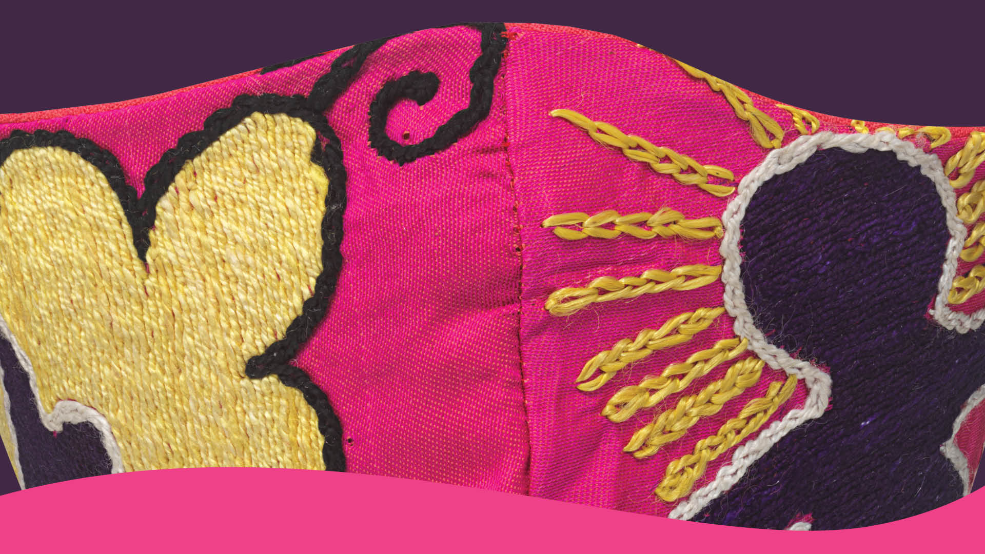 Detail of pink cloth mask with embroidered figures in black and yellow.